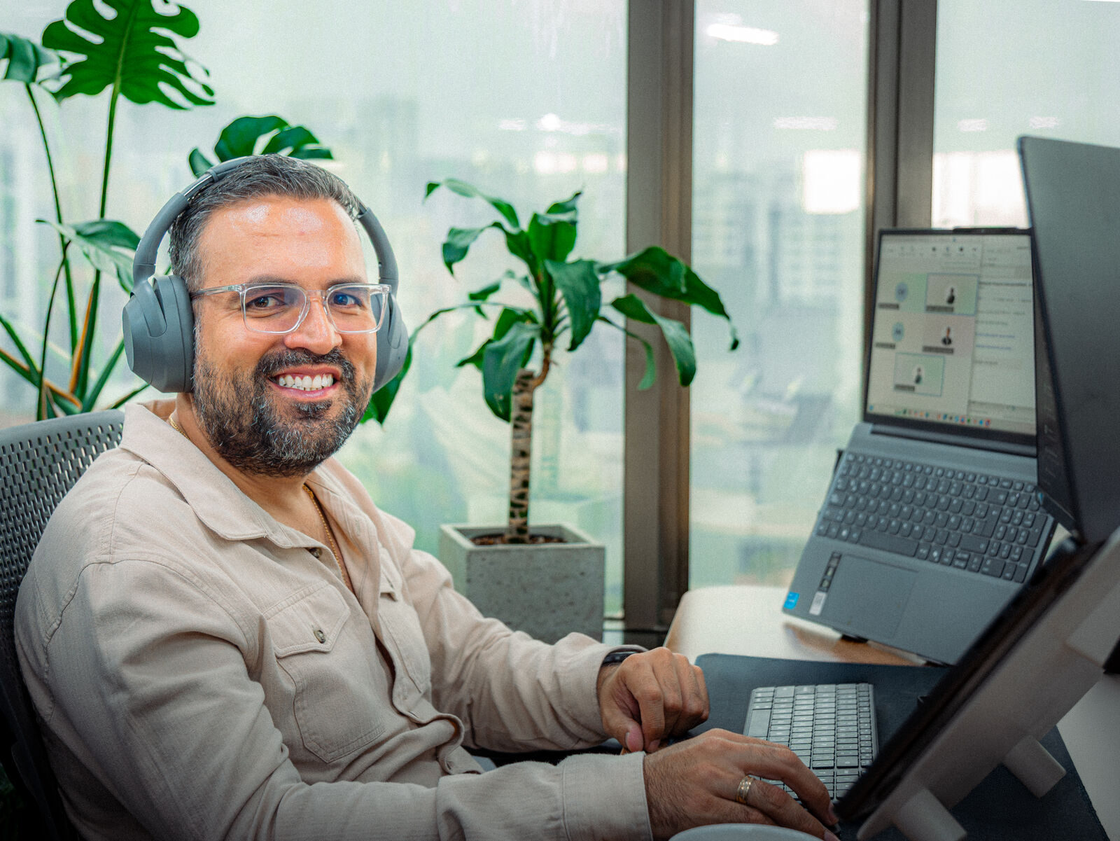 Engineer with headphones smiling at his desk surrounded by office plants.
